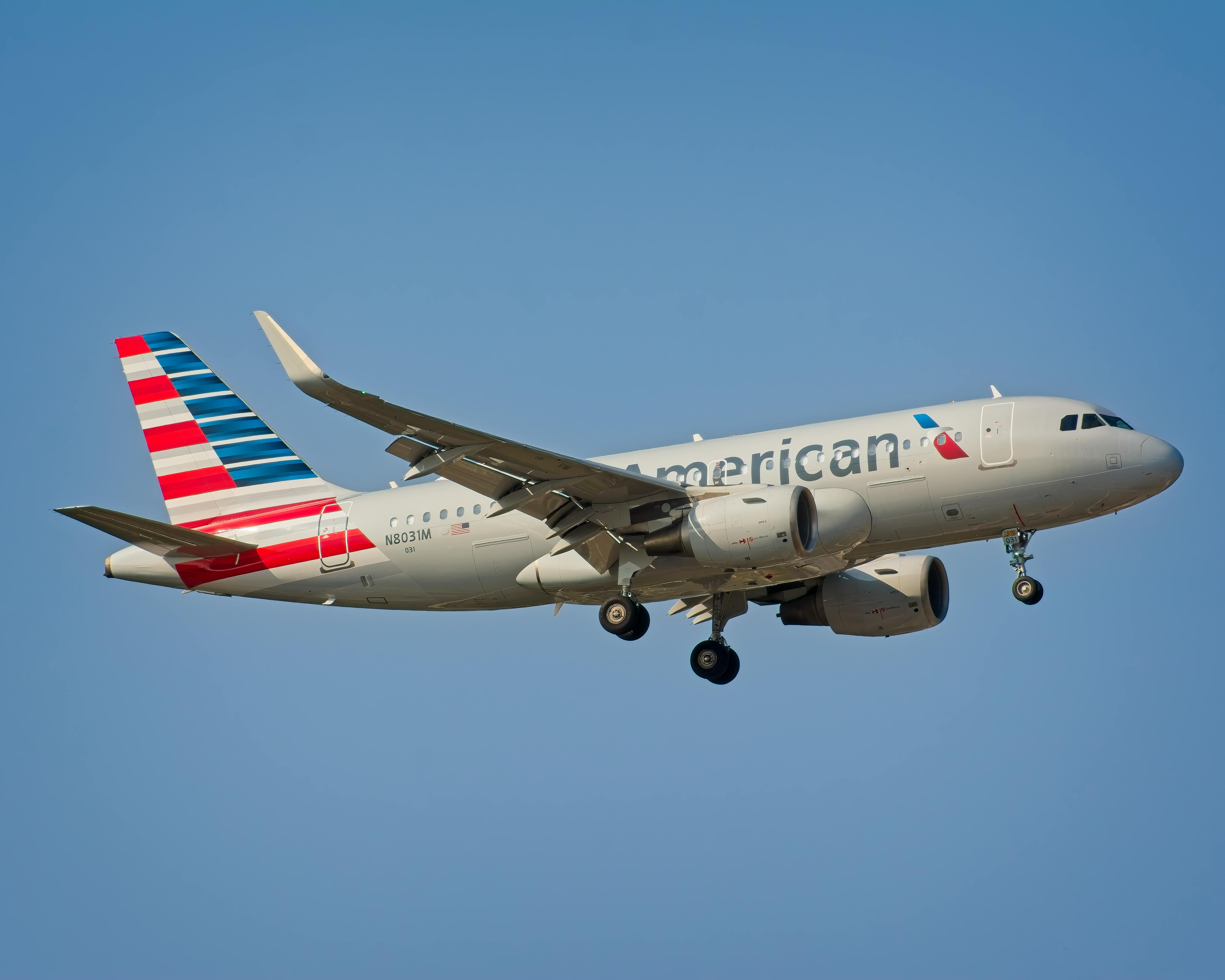 American Airlines Airbus A319 airplane landing under clear sky in New York City.