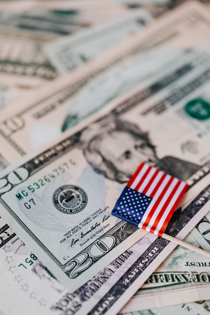 services-img From above composition of tiny American flag placed on pile of United States dollar bills as national currency for business and personal financial operations